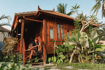 Canvas Print - Young and elegant couple sitting in front of their beautiful wooden country house in Bali, Ubud