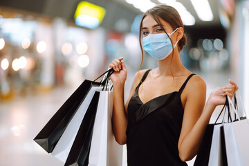 Woman in shopping. Young woman in protective sterile medical mask on her face with shopping bags in the mall. Purchases, black friday, discounts,  sale concept. Covid-2019.