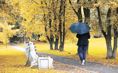 A young man in glasses walks in the park with an umbrella during the rain.