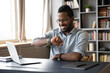 Smiling African American businessman wearing glasses checking time, looking at wristwatch on hand, positive happy young man entrepreneur sitting at desk, planning work, task management concept