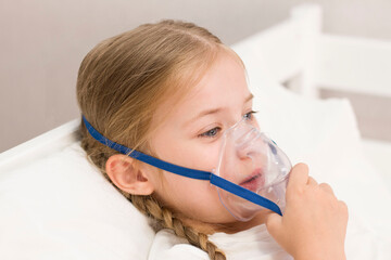 girl is breathing through an inhaler. a sick child is lying on the bed