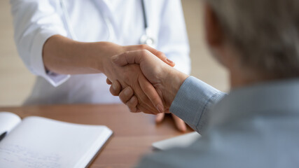 Wall Mural - Close up young woman doctor shaking mature patient hand, greeting at medical appointment in hospital, acquaintance, senior man thanking physician therapist gp for treatment, making agreement