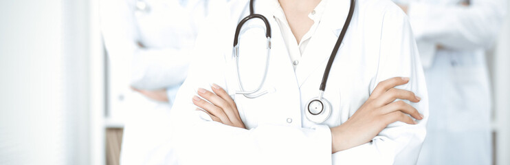 Unknown woman-doctor standing straight with arms crossed in clinic, close-up. Medical team ready to stop coronavirus pandemic. Medicine concept