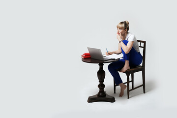 Focused young female student sitting at desk working or studying remotely online writing notes while looking on laptop screen. Distant learning or remote work from home. Isolated on white background.