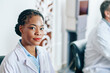 © DragonImages - Portrait of serious young Black female doctor in labcoat looking at camera