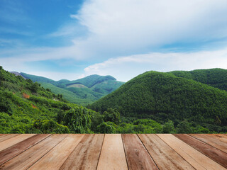 Wooden table top over green mountain range over blue sky background.