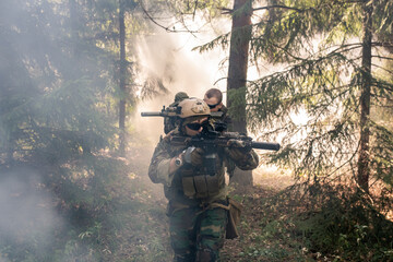 Group of armed soldiers in camouflage outfits holding rifles and getting across foggy forest