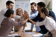 © fizkes - Happy international group of different generations business people, joining hands over table in high five gesture, celebrating common corporate success or involved in motivating team building activity