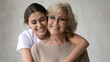 © fizkes - Head shot portrait of sincere smiling young arabic ethnicity woman cuddling happy middle aged 60s mother in glasses. Different generations mixed race family bonding, showing love looking at camera.