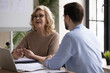 © fizkes - Overjoyed middle aged senior female leader having fun, enjoying informal conversation with young male colleague at office meeting. Happy mature mentor laughing at funny joke with partner indoors.