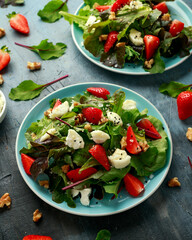 Wall Mural - Goats cheese and strawberry summer salad served with nigella and sesame seeds drizzled with runny honey