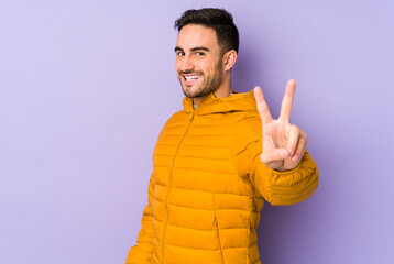 Young caucasian man isolated on purple background joyful and carefree showing a peace symbol with fingers.