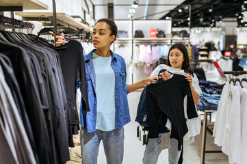 Canvas Print - Girls take clothes on hangers in clothing store