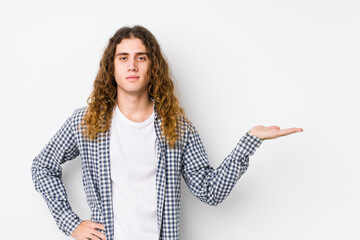 Wall Mural - Young long hair man posing isolated showing a copy space on a palm and holding another hand on waist.