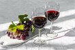 © Caterina Trimarchi - Two wineglass with red wine and ripe pink grapes on white table in the garden in the sunny day.