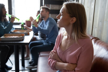 Upset offended young woman sitting separately, apart from diverse friends in cafe close up, sad excluded female feeling outsider, bad friendship concept, problem with communication, social outcast