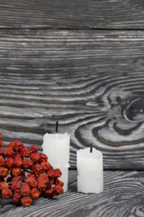 Two candlesticks on brushed pine boards. Nearby is a dried rowan bunch.