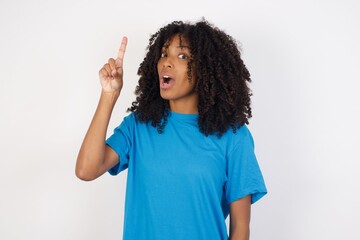 Wall Mural - Young african woman with curly hair wearing casual blue shirt over white background pointing finger up with successful idea. Exited and happy. Number one.