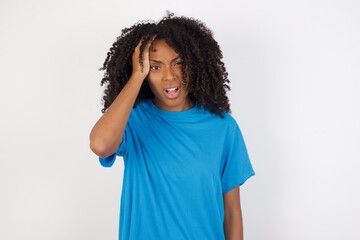 Wall Mural - Embarrassed attractive Young african woman with curly hair wearing casual blue shirt, with shocked expression, expresses great amazement, Puzzled woman poses indoor