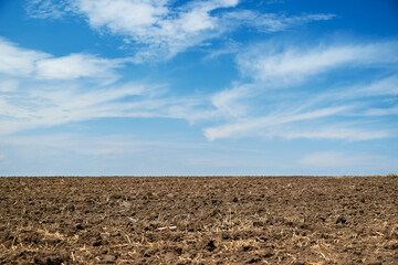 plowed field and blue sky, soil and clouds of a bright sunny day - concept of agriculture