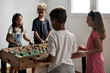 © Alex Tihonov - Group of multi cultural cute children stand indoor spend playtime with friends playing foosball together. Tabletop version of soccer lovers. Having fun and recreation of alpha generation kids concept