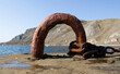An old rusty metal device for mooring a boat on a pier with a sea and mountain background.