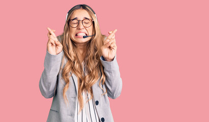 Young beautiful blonde woman wearing call center agent headset gesturing finger crossed smiling with hope and eyes closed. luck and superstitious concept.