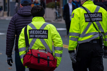 Medical first responders walking along a road wearing black wool stocking caps, yellow reflective coats with medical first responder in grey letters.