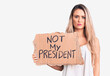 © Krakenimages.com - Young beautiful blonde woman holding not my president cardboard banner thinking attitude and sober expression looking self confident