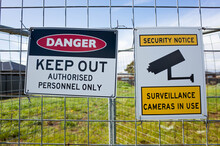 The Sign Of 'Danger Keep Out Authorised Personnel Only' And ' Security Notice Surveillance Cameras In Use' On A Metal Construction Barrier By A Lot Of Private Vacant Land. Concept Of No Trespassing.