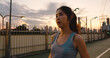 Beautiful young Asian athlete lady exercises because feel tired after running in urban environment. Japanese teen girl work out wearing sports clothes on walkway bridge in early morning.