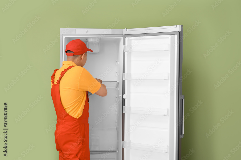 Worker repairing fridge on color background