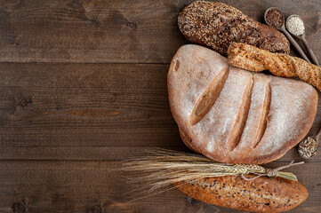 Wall Mural - The bakery, several different fresh loaves of bread with a crisp crust, sprinkled with seeds and sesame seeds on a wooden background with boils of wheat.