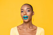 Close up portrait of amazed young African American woman with fashionable colorful make up looking at camera isolated on yellow studio background