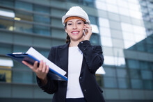 Young Woman Engineer In Suit And Hat Is Talking About Project By The Phone Near The Building.