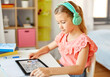 © Syda Productions - education, e-learning and school concept - happy student girl in headphones with teacher on tablet computer having online lesson at home desk