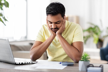 Poster - remote job, technology and people concept - unhappy young indian man with calculator and papers working at home office