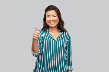 people, gesture and portrait concept - happy asian young woman showing thumbs up over grey background