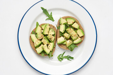Wall Mural - Avocado slices on whole grain bread with arugula. Healthy vegetarian breakfast concept. White background, top view