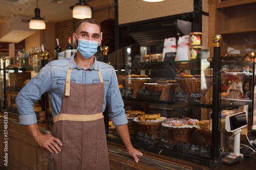 Fotomural Male baker wearing medical face mask working at his bakery store during coronavi