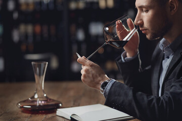 Sommelier compiles tasting card of alcohol for restaurant, evaluates red wine in glass