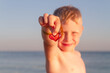 The boy is holding a red glass heart. A European child 6 years old is resting on the sea.