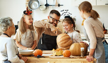 Happy Family Mother, Father, Grandmother And Children Prepare For Halloween By Carving Pumpkins At Home In Kitchen.