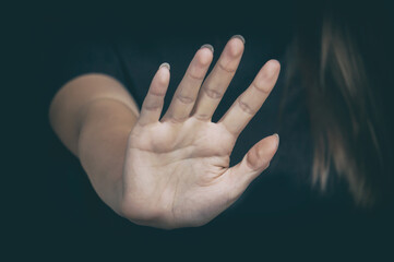 A woman's hand with a stop gesture on a dark background. Copy space, selective focus