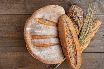 Wall Mural - The bakery, several different fresh loaves of bread with a crisp crust, sprinkled with seeds and sesame seeds on a wooden background with ears of wheat.