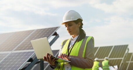 portrait of electrician engineer in safety helmet and uniform using laptop checking solar panels. fe