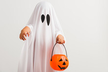 Funny Halloween Kid Concept, Little Cute Child With White Dressed Costume Halloween Ghost Scary He Holding Orange Pumpkin Ghost On Hand, Studio Shot Isolated On White Background