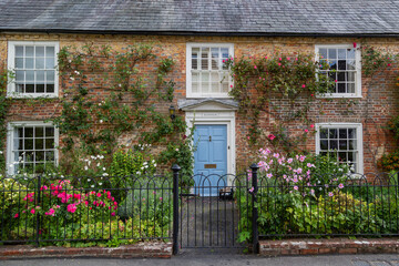 the exterior of an english cottage with flowers blooming in the front garden and sash windows, a typ