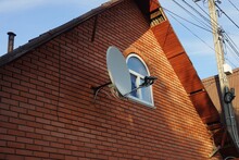 Attic Of A Red Brick House With A Small White Window And A Satellite Dish
