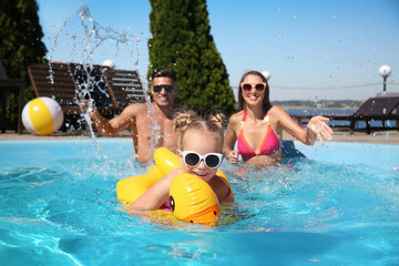 Wall Mural - Little girl swimming with inflatable ring near her parents in outdoor pool on sunny summer day